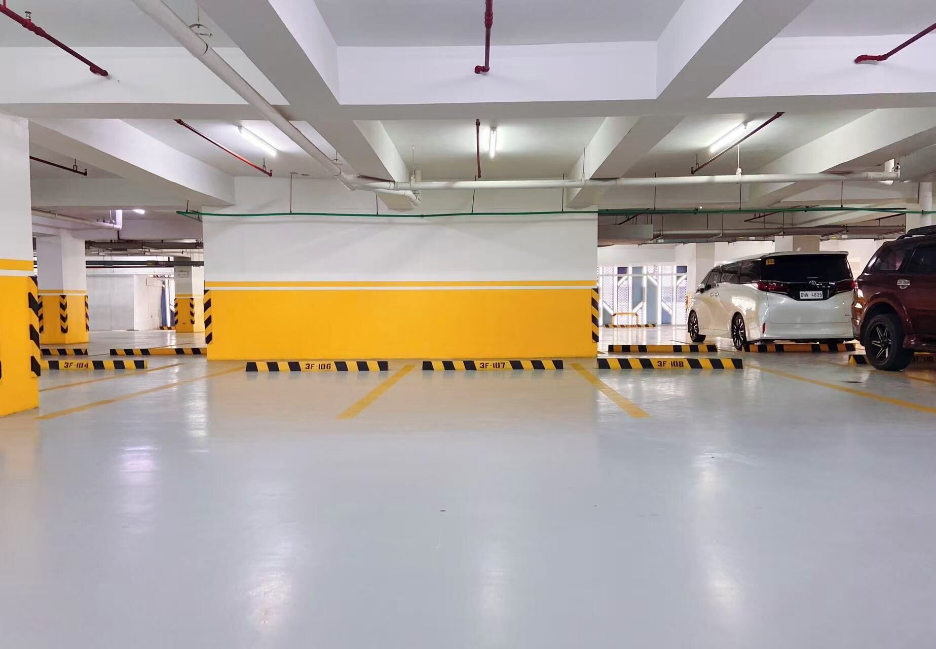 A multi-level parking garage with yellow and black striped barriers, white walls, and fluorescent lighting.