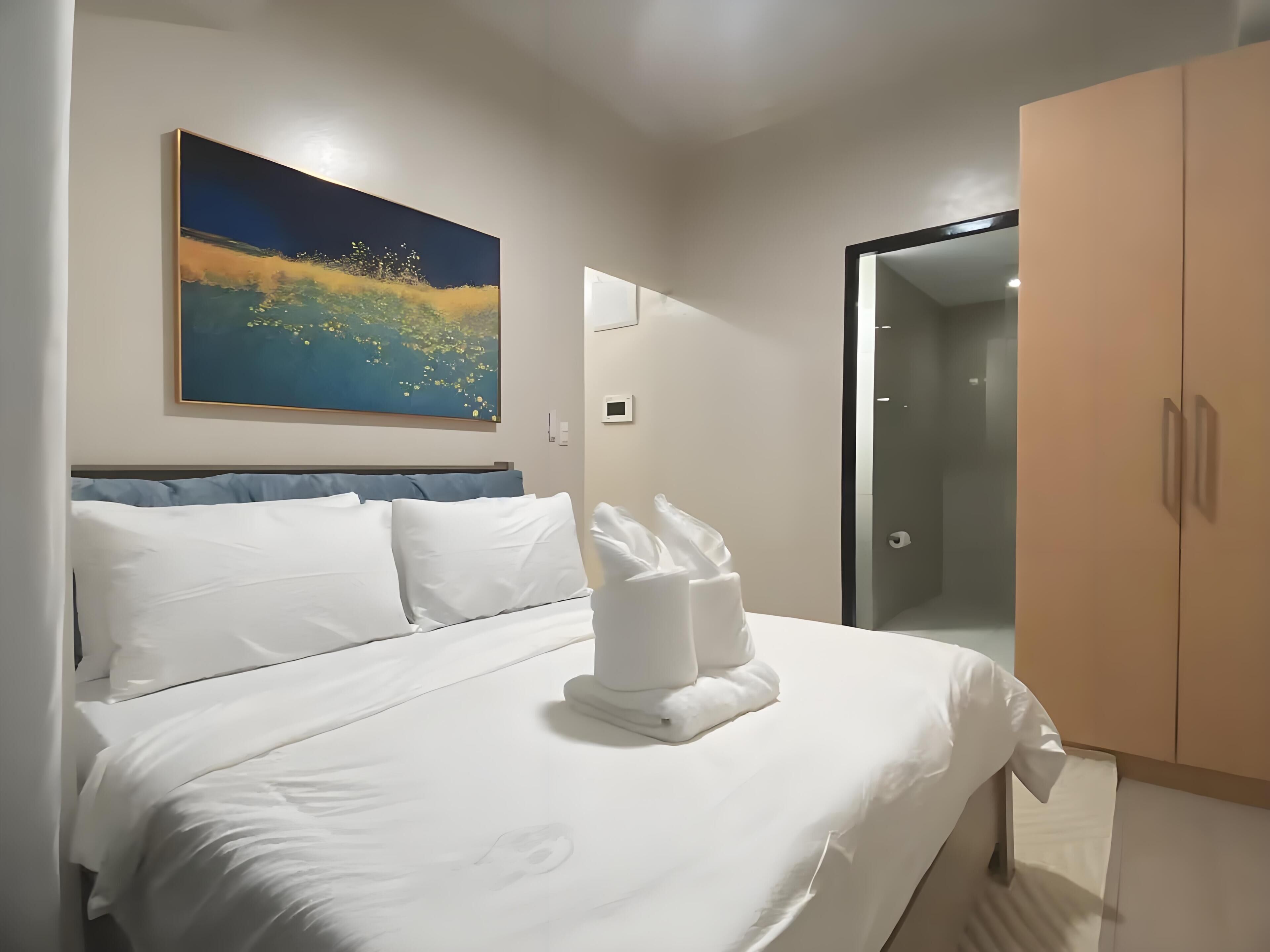 A hotel room with a bed, a painting, a wardrobe, and a bathroom door.