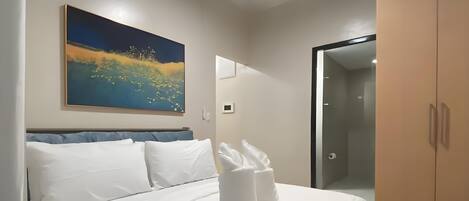 A hotel room with a bed, a painting, a wardrobe, and a bathroom door.