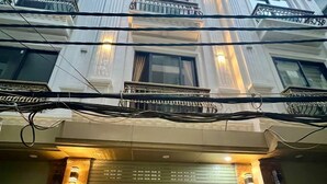 Un immeuble à plusieurs étages doté d’une entrée centrale, avec une grande porte en bois, deux motos garées devant et un balcon orné de rampes en métal.