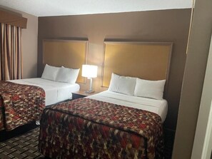 Une chambre d’hôtel avec deux lits, une table de chevet avec une lampe et un tapis à motifs.