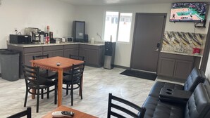 A compact kitchen with a dining area, a sofa, and a TV mounted on the wall.