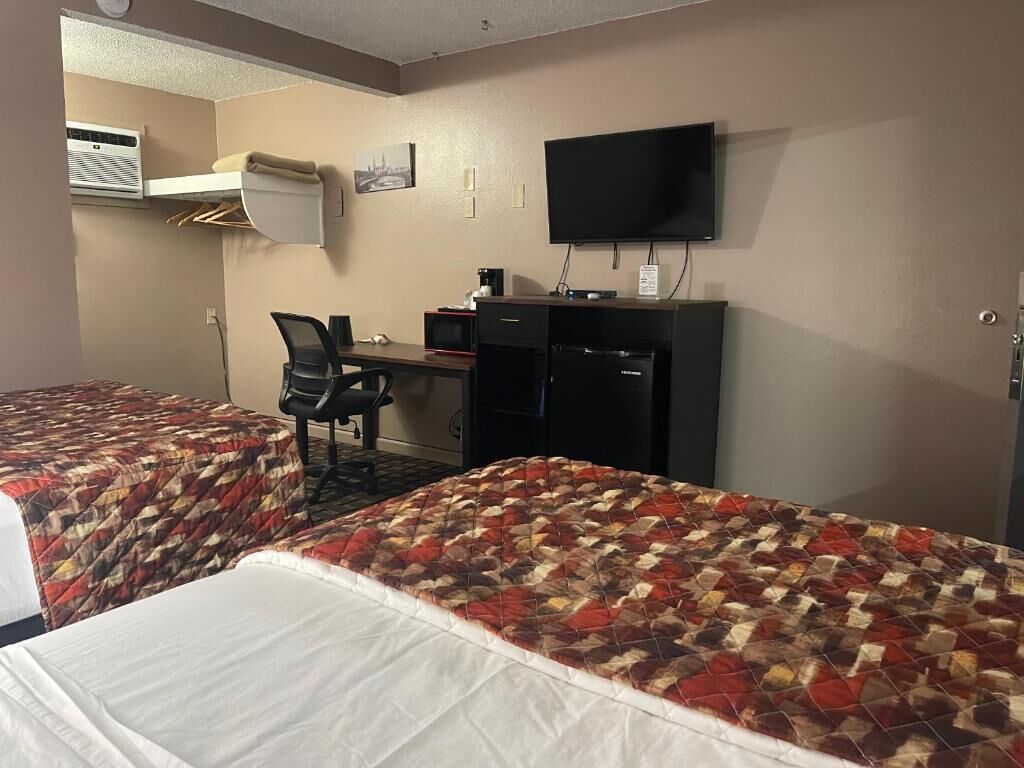 A hotel room with two beds, a desk with a computer, a television, and an air conditioning unit.