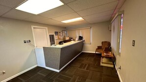 A reception area with a desk, chairs, a bulletin board, and a window with blinds.