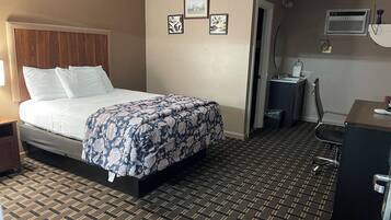 Habitación de hotel con cama, escritorio, silla, equipo de aire acondicionado y puerta que da a otra habitación.