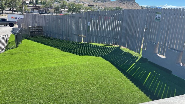 A fenced area with artificial grass, a wooden fence, and a mountain backdrop.