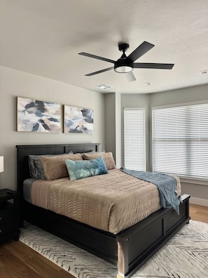 Un dormitorio con cama, ventilador de techo, obras de arte y ventanas.