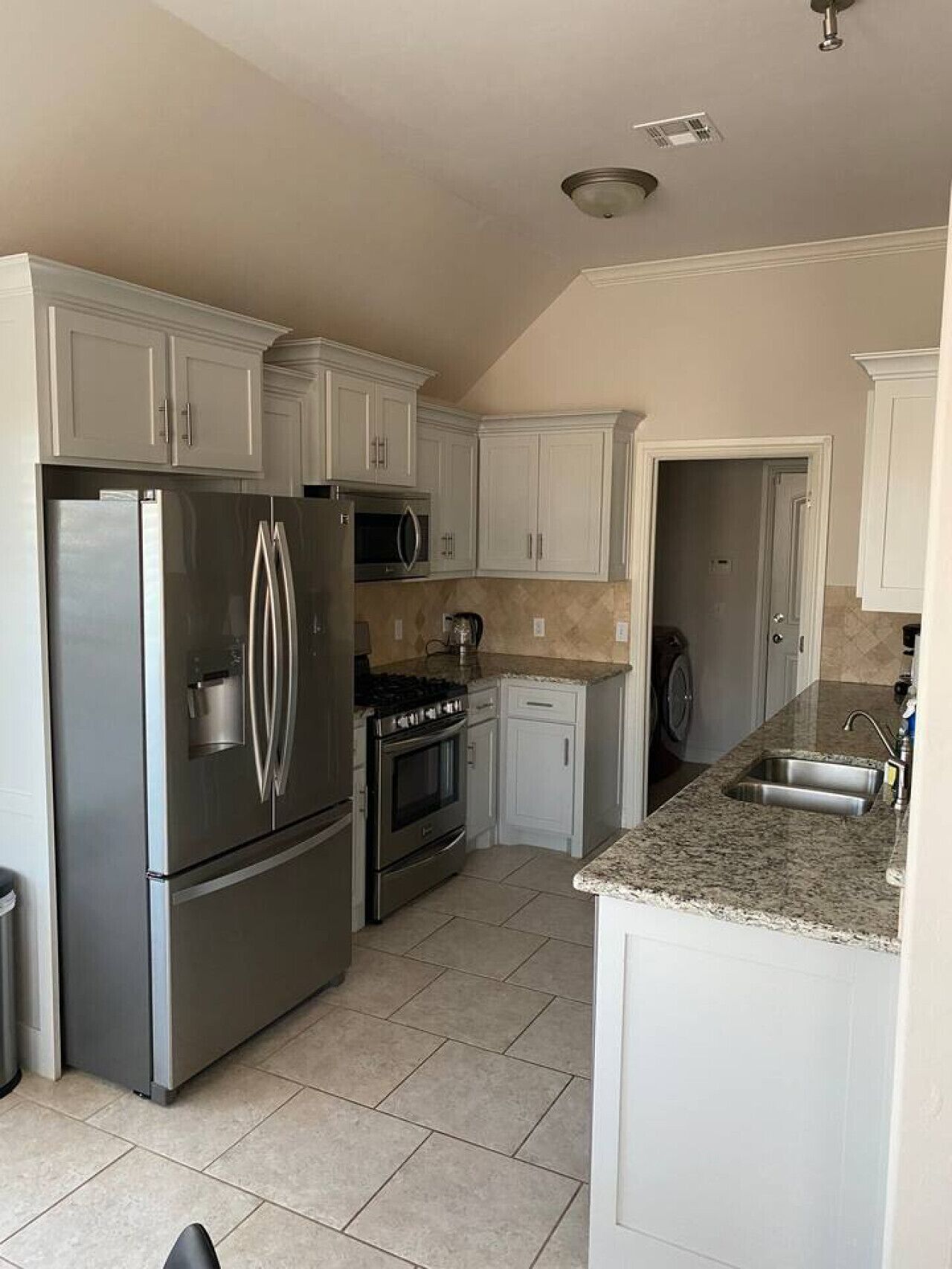 A kitchen with white cabinets, stainless steel appliances, a granite countertop, and a tiled floor.