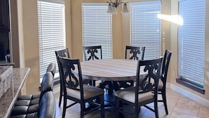 A dining area with a round table, six chairs, a chandelier, and large windows with blinds. - `Live Like a Local, Stay Like a Guest` (Oklahoma City)