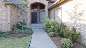 A brick house with a front door, a small front yard with shrubs, and a pathway leading to the door. - `Live Like a Local, Stay Like a Guest` (Oklahoma City)