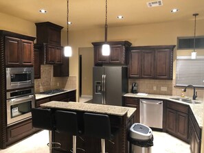 Une cuisine moderne avec des meubles en bois foncé, des appareils en acier inoxydable, un plan de travail en granit et des luminaires suspendus.