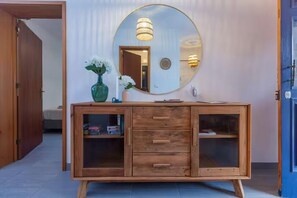A wooden vanity with a mirror, a vase with flowers, and a cabinet with drawers and shelves. - Silke House (Vila Franca Do Campo)