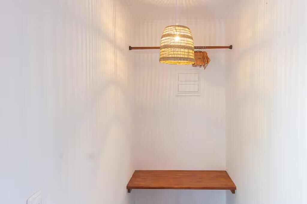 Una stanza con uno scaffale in legno, una lampada a sospensione e una parete bianca.