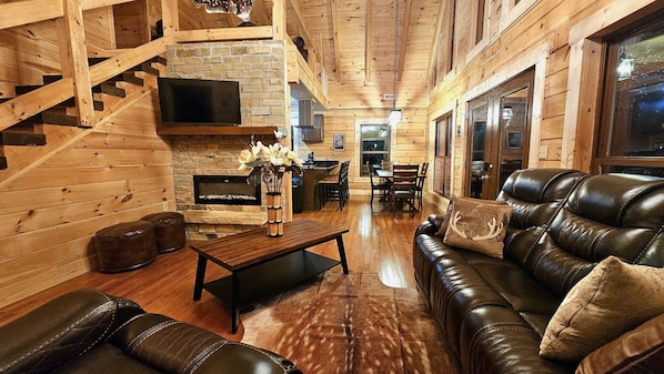 A log cabin interior with a fireplace, leather furniture, and a dining area.