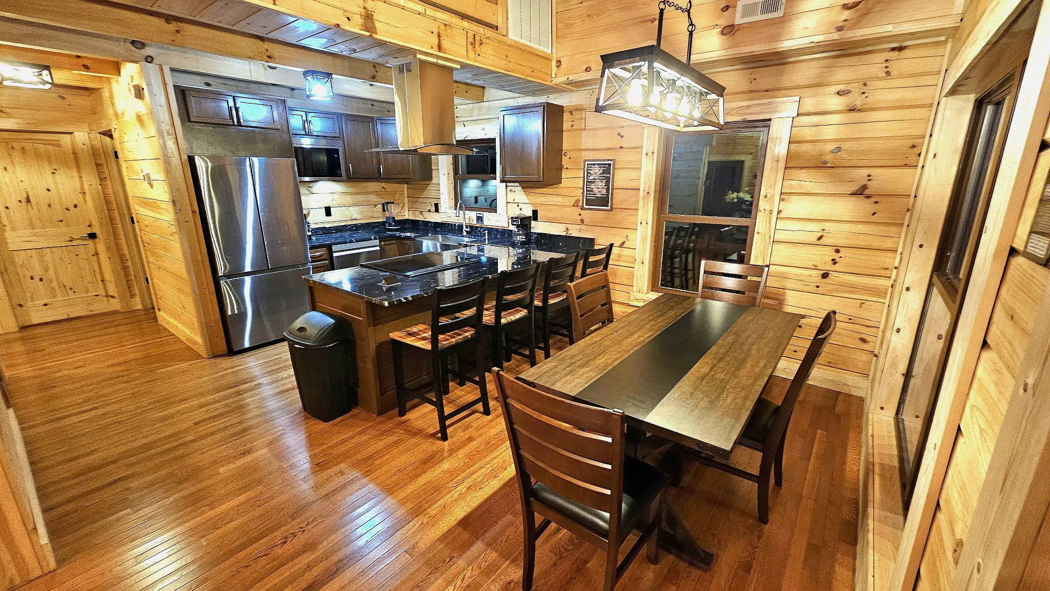 A wooden cabin interior with a kitchen, dining area, and a large window.