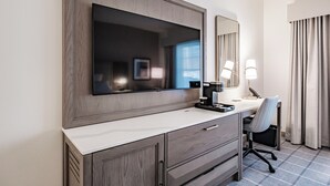 A hotel room with a large mirror, a flat-screen TV, a desk with a chair, and a window with curtains. - Hotel Bridgton (Bridgton)