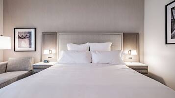 A hotel room with a large bed, two bedside tables, a nightstand, a chair, and framed pictures on the walls.