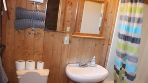 A wooden bathroom with a toilet, sink, and shower curtain.