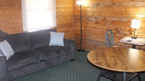 A room with a sofa, a round wooden table, a floor lamp, and a window with blinds.