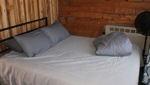 A bed with a headboard, two pillows, a white bedspread, and a wall with wooden paneling.