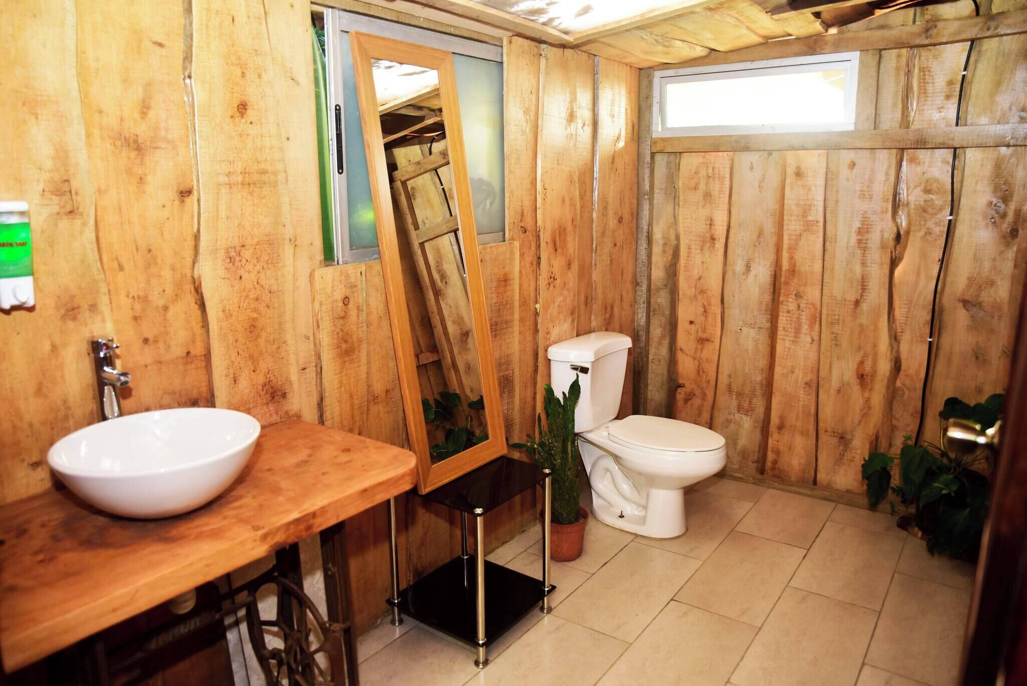 Une salle de bain aux murs lambrissés, équipée d’un lavabo, de toilettes et d’un miroir.