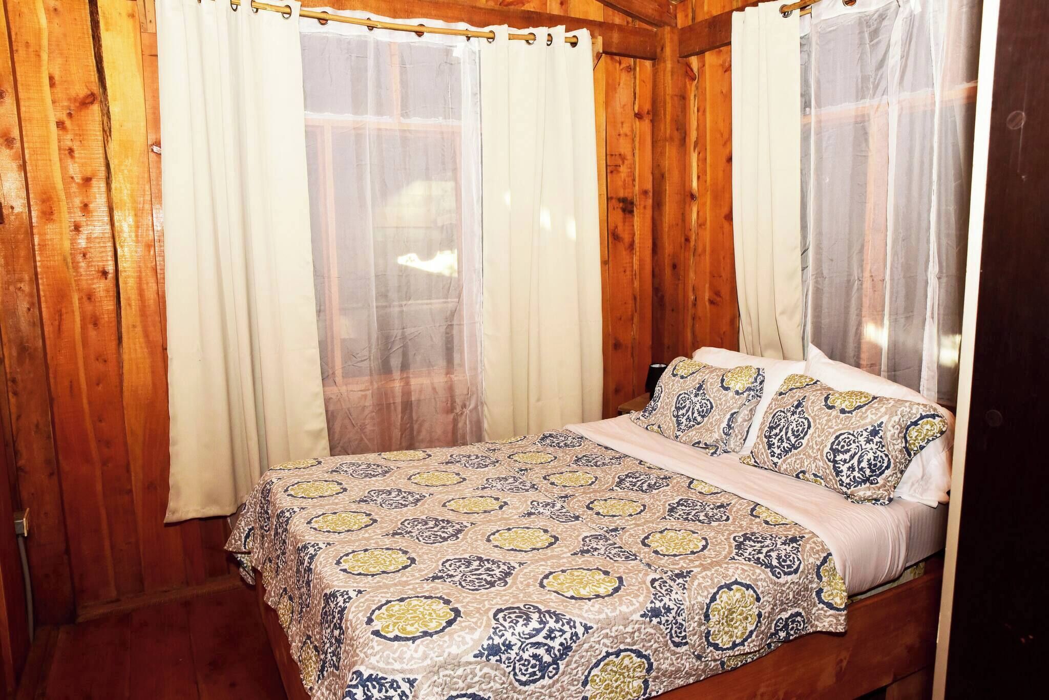 A wooden room with a bed, curtains, and a window.