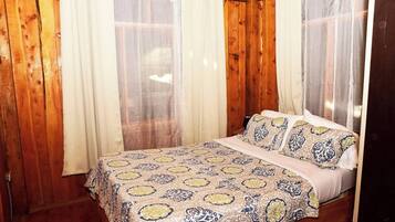 A wooden room with a bed, curtains, and a window.