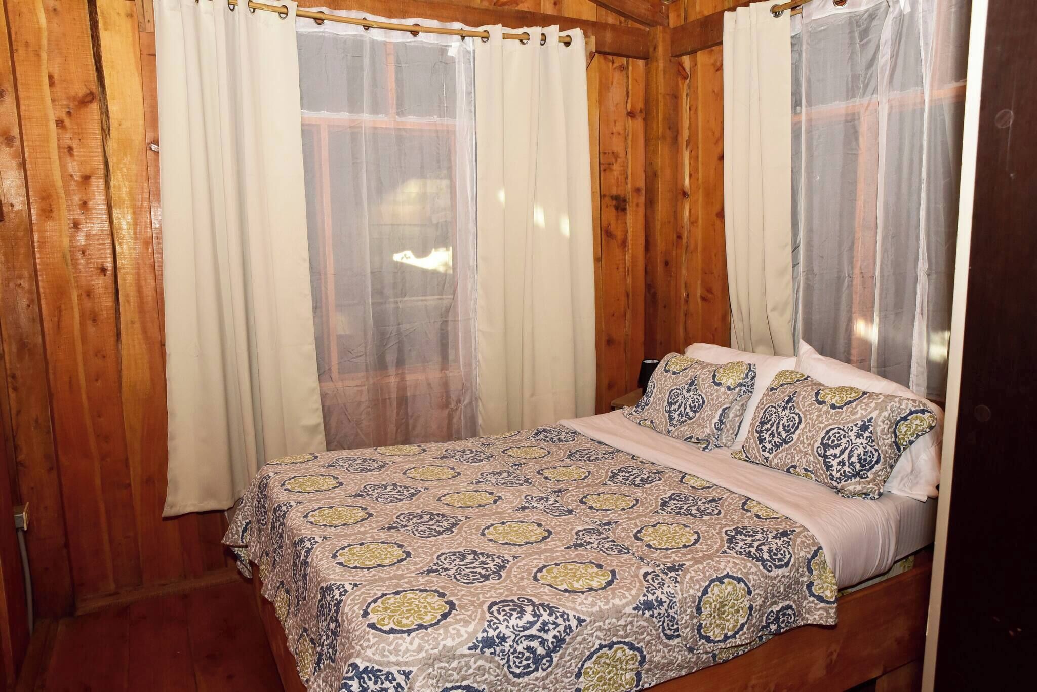 Ein Zimmer mit Holzboden, einem Bett, Vorhängen und einem Fenster.