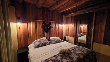 Una habitación de madera con una cama, un macramé colgante y un espejo.