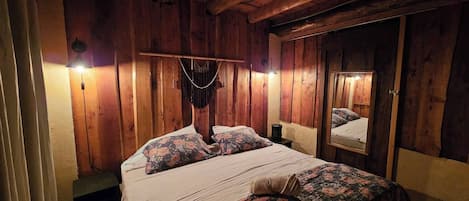 A wooden room with a bed, a hanging macrame, and a mirror.