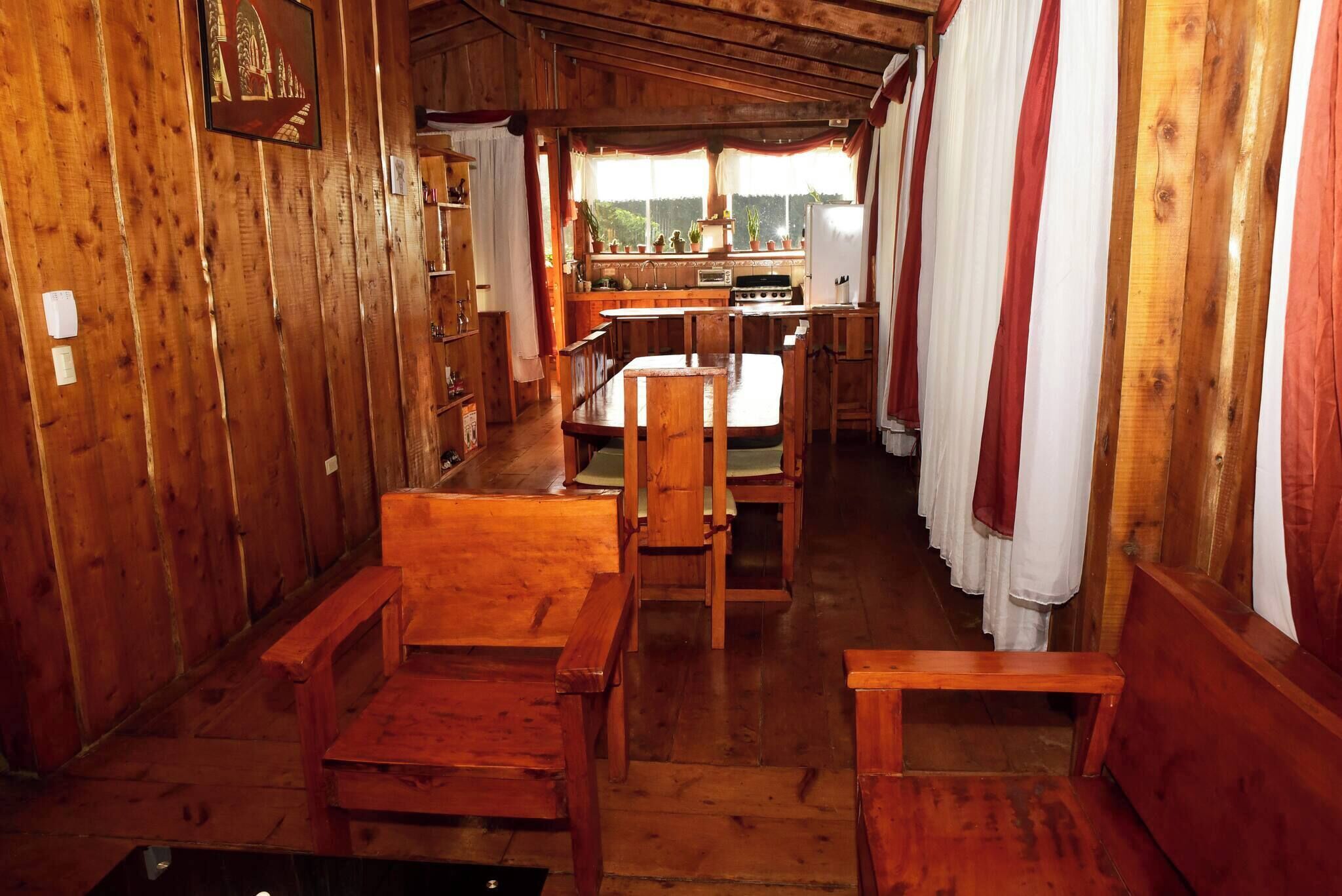 Un interior de madera con comedor, cocina y una ventana con cortinas.