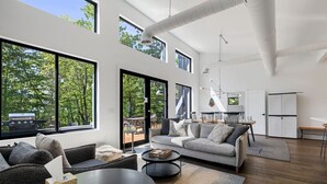 Amplia sala de estar con ventanas grandes, un sofá, una mesa de centro y un comedor con sillas.