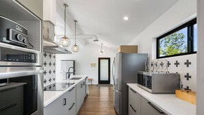 Una cocina moderna con electrodomésticos de acero inoxidable, una isla central, iluminación colgante y vistas a través de una ventana.