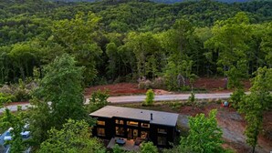 Una casa moderna con una amplia terraza, rodeada de un bosque denso y montañas al fondo.