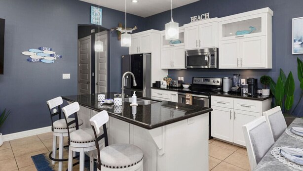 Una cocina moderna con armarios blancos, una isla central y una zona de comedor con taburetes de bar.