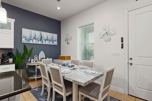 Ein Essbereich mit einem Tisch für vier Personen, eine Küche mit Kaffeemaschine und ein großes Gemälde an der Wand.