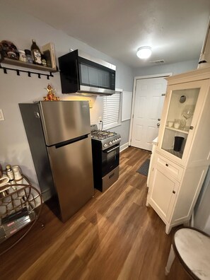 A compact kitchen with a refrigerator, stove, microwave, and white cabinetry.
