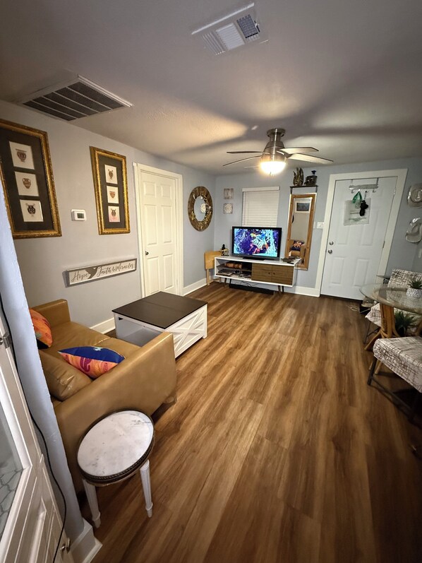 A living room with a TV, a sofa, a coffee table, and a dining area with a table and chairs.