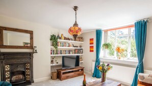 Ein Wohnzimmer mit Kamin, Fernseher, Bücherregal und einem Fenster mit Vorhängen.