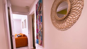 Ein Korridor mit Holzboden, einem Bett mit orangefarbener Bettwäsche und einem an der Wand befestigten Spiegel.