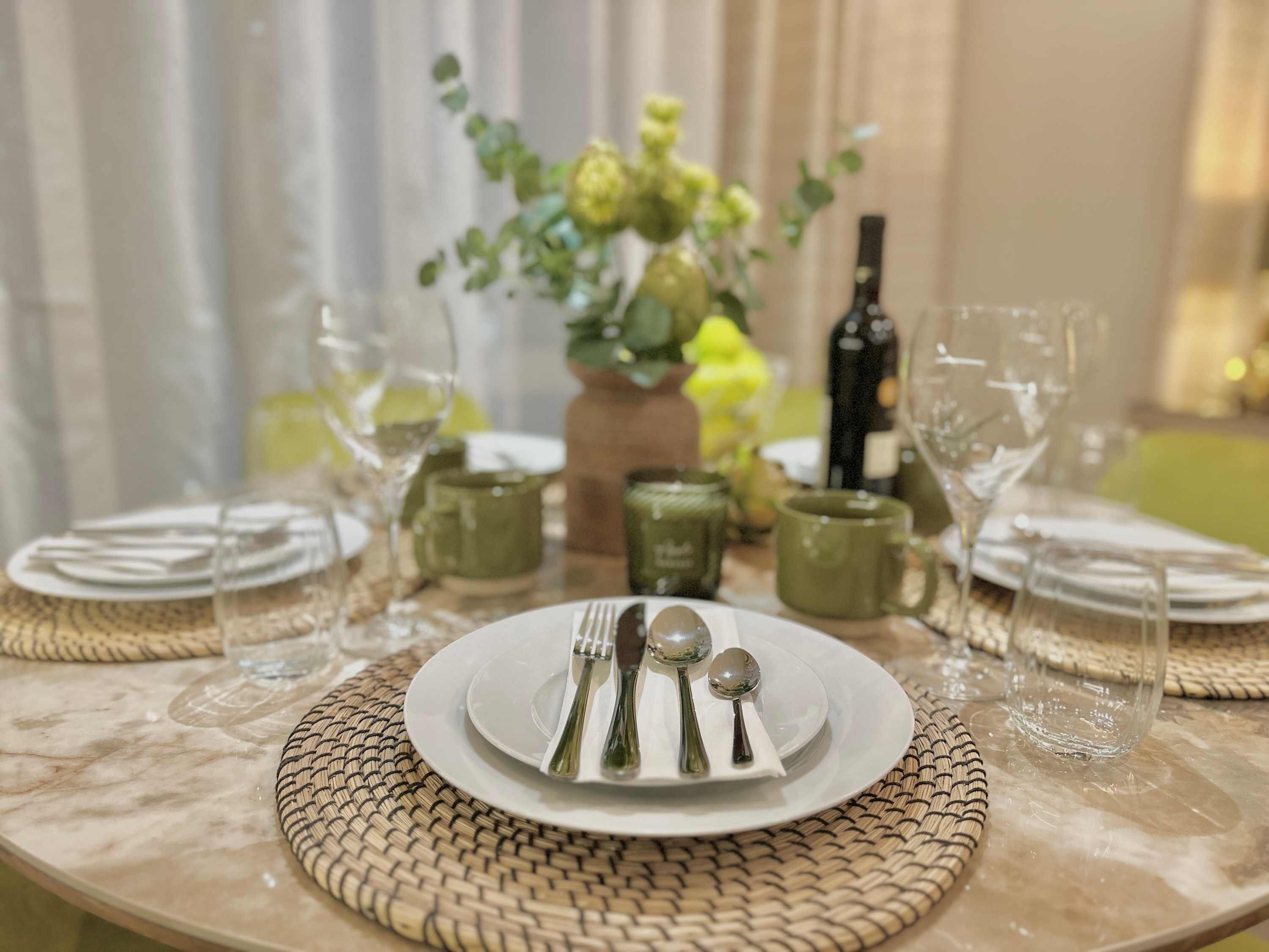 A table set with plates, cutlery, and glasses, with a vase of flowers and a bottle in the background.