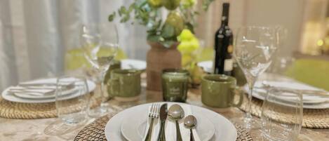 A table set with plates, cutlery, and glasses, with a vase of flowers and a bottle in the background.
