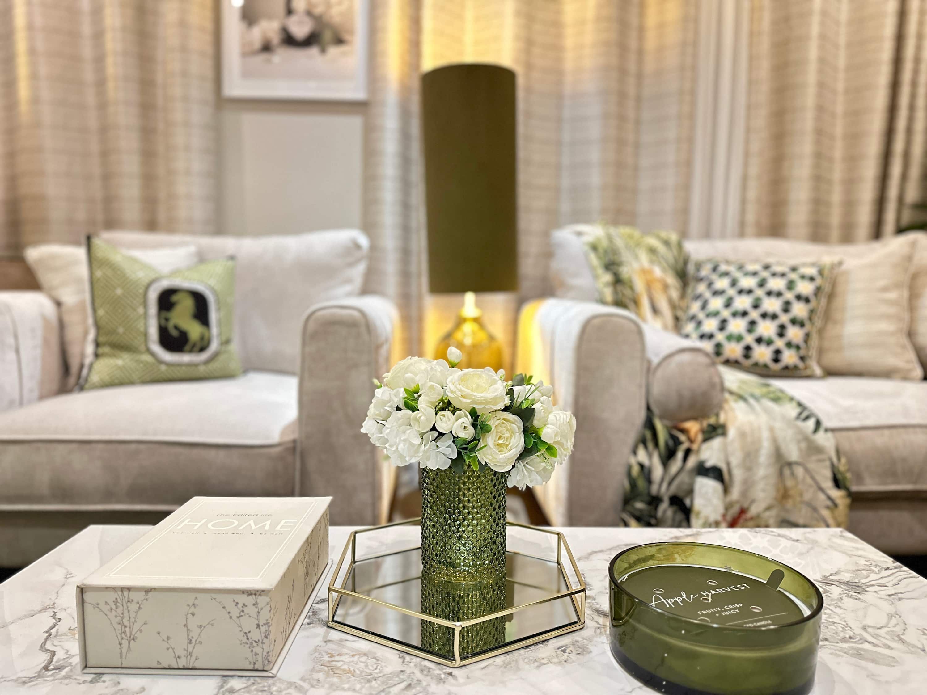 Un salon avec un canapé, un vase de fleurs blanches, une bougie et une boîte posée sur une table.