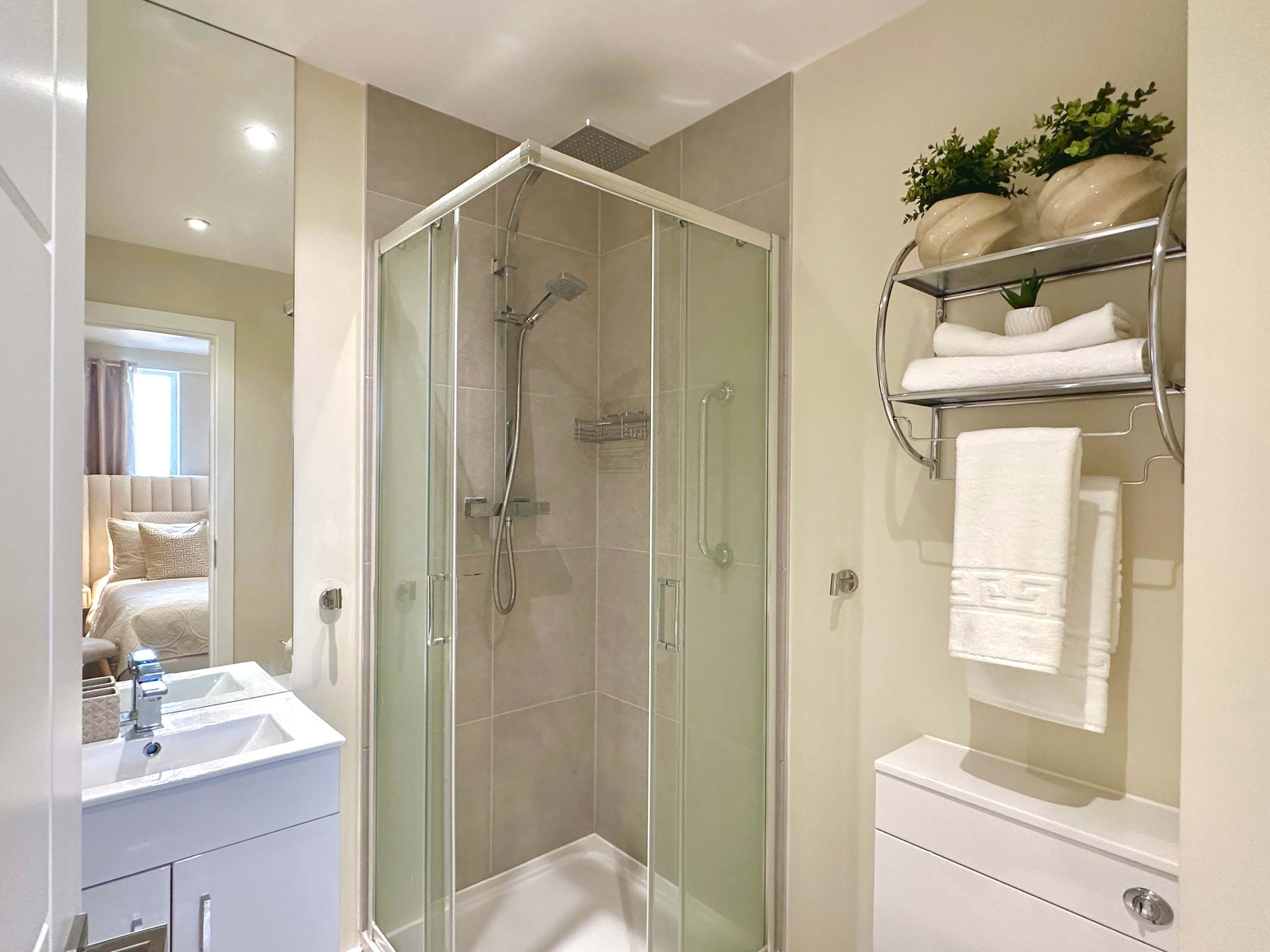 Une salle de bain moderne avec une douche à parois de verre, un lavabo blanc et un porte-serviettes où sont soigneusement pliées les serviettes.