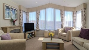 A modern living room with a fireplace, a flat-screen TV, and a sofa set. - Pheasant Lodge (Holyhead)