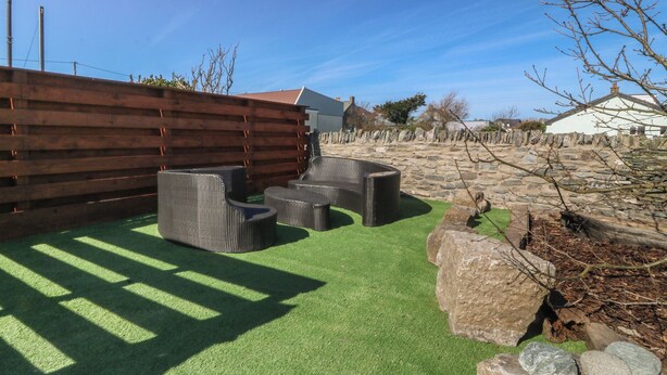 A patio with outdoor furniture, a wooden fence, and a stone wall. - Pheasant Lodge (Holyhead)