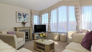 A living room with a fireplace, a flat-screen TV, and a sofa. - Pheasant Lodge (Holyhead)