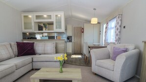 A modern living room with a sofa, a coffee table, and a kitchen in the background. - Pheasant Lodge (Holyhead)