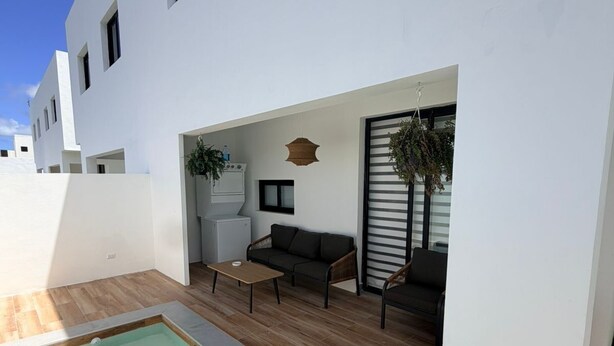 Un'area esterna moderna con piscina, pavimento in legno, un divano e un tavolo da pranzo.