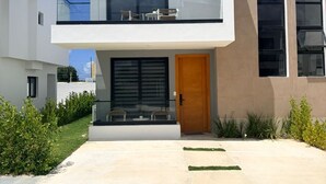 Una casa moderna su due piani, con un balcone, un'entrata e un piccolo spazio esterno con posti a sedere.